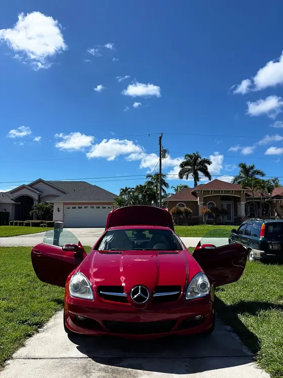 Red Mercedes SLK 350 with doors open under a bright Florida sky
