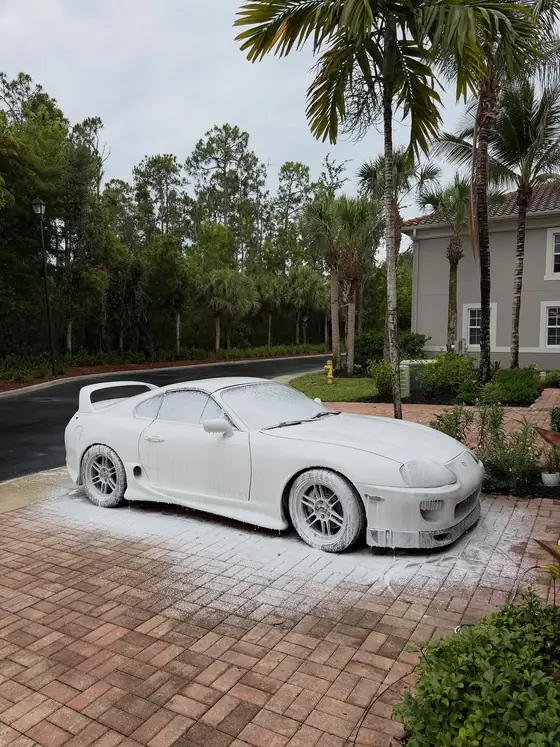 Mk4 Toyota Supra fully covered in white snow foam under palm trees