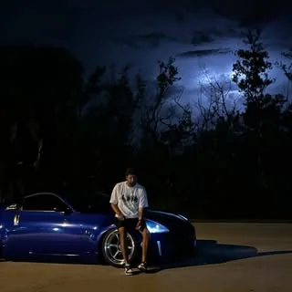 Tarek Ezzo sitting on his blue Nissan 350Z at night under a lightning sky